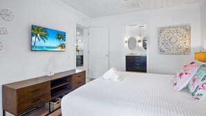 Un dormitorio con una cama, un aparador, un cuadro de una playa, un espejo y un adorno de pared.