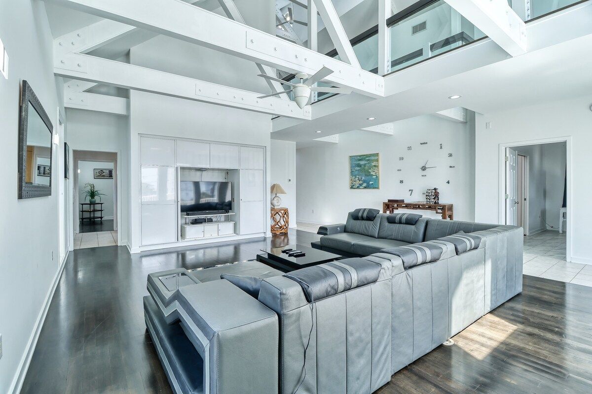 A modern living room with a large grey sectional sofa, a flat-screen TV, and a ceiling fan.