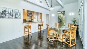 A modern kitchen with wooden cabinets, a stainless steel range hood, and a dining area with a glass table and wicker chairs. - Wow By The Sea (North Myrtle Beach)