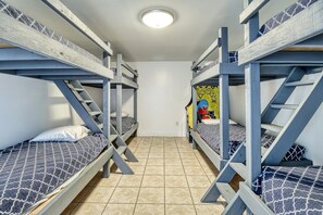 A dormitory room with bunk beds, a tiled floor, and a ceiling light.
