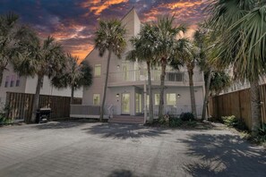 A two-story building with a balcony, surrounded by palm trees, and a paved driveway.