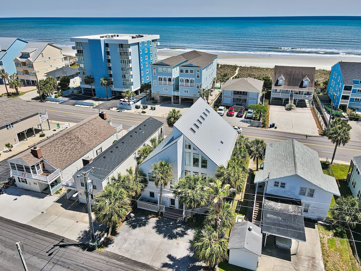 A coastal residential area with beachfront properties, including a multi-story building with balconies and a single-story house with a garage.