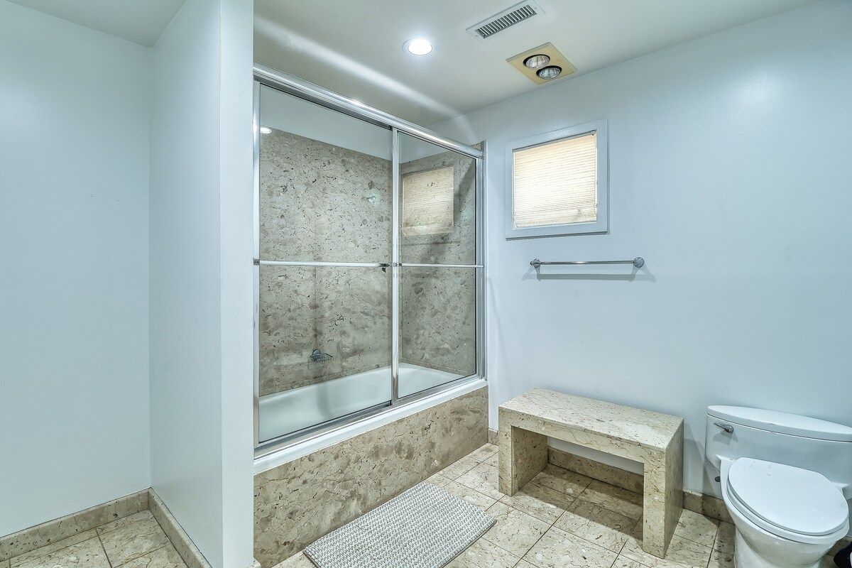 A bathroom with a glass-enclosed shower, a toilet, and a bench.