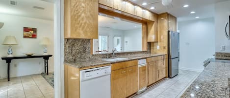 Una cocina moderna con gabinetes de madera, encimeras de granito, lavavajillas y refrigerador.