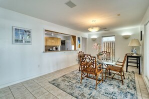 A dining area with a glass table and wooden chairs, a kitchen in the background, and a window with a view. - Pet/Student Friendly, Ocean Blvd (North Myrtle Beach)
