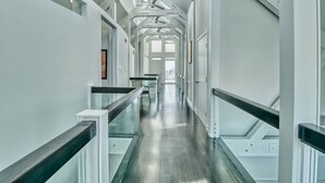 A modern, spacious hallway with a glass railing, metal beams, and a ceiling fan. - Wow By The Sea (North Myrtle Beach)