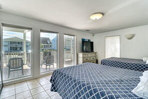 A hotel room with two beds, a television, and a balcony with chairs.