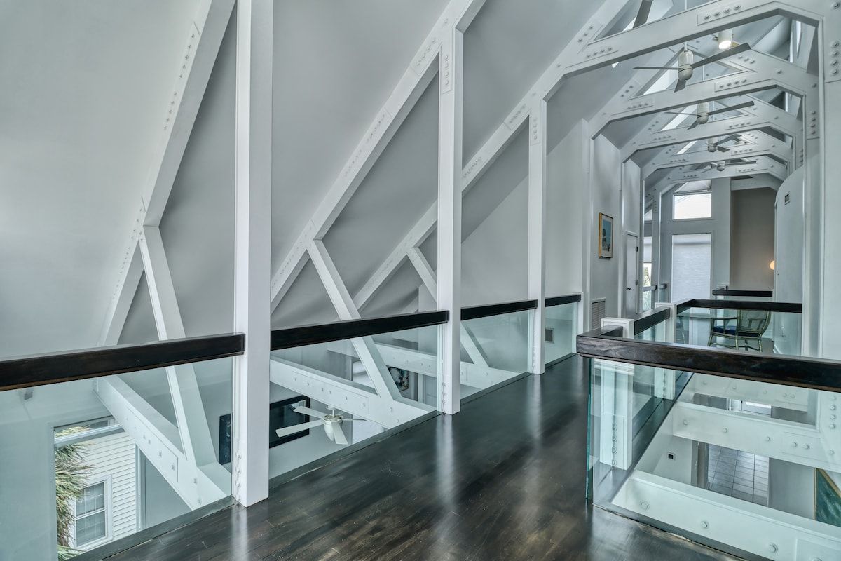 Et moderne interiør med glasgelænder, hvide konstruktionsbjælker og mørkt gulv.