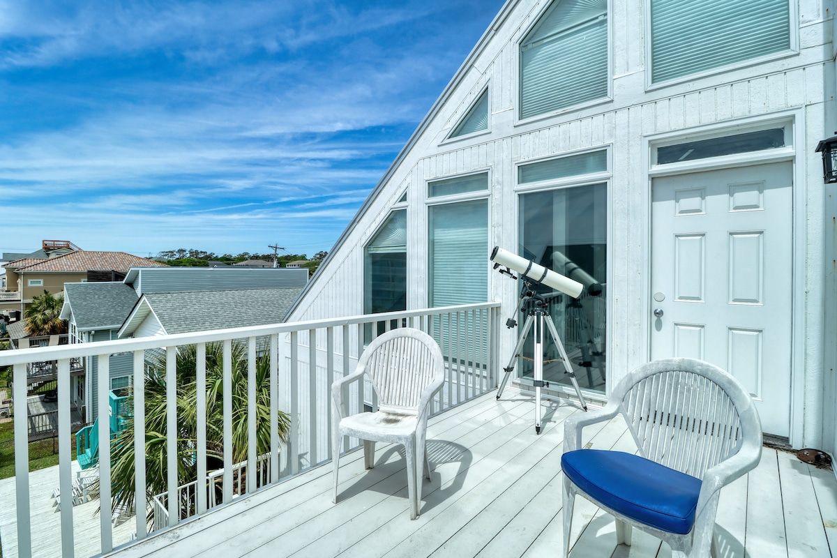 Un balcon avec un télescope, deux chaises et une porte blanche.