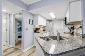 Une cuisine moderne dotée de plans de travail en granit, d’appareils électroménagers en acier inoxydable et de meubles blancs.