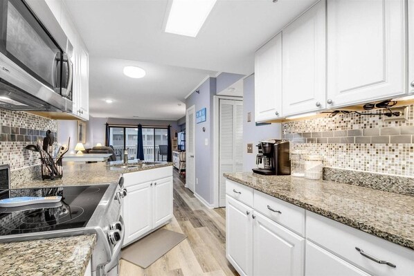 A modern kitchen with white cabinets, granite countertops, and a built-in stove.