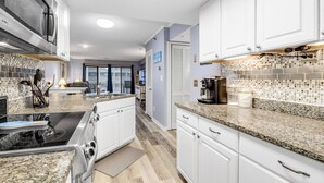 A modern kitchen with granite countertops, white cabinetry, and a built-in oven. - Sunset at Sassy's 2 (North Myrtle Beach)