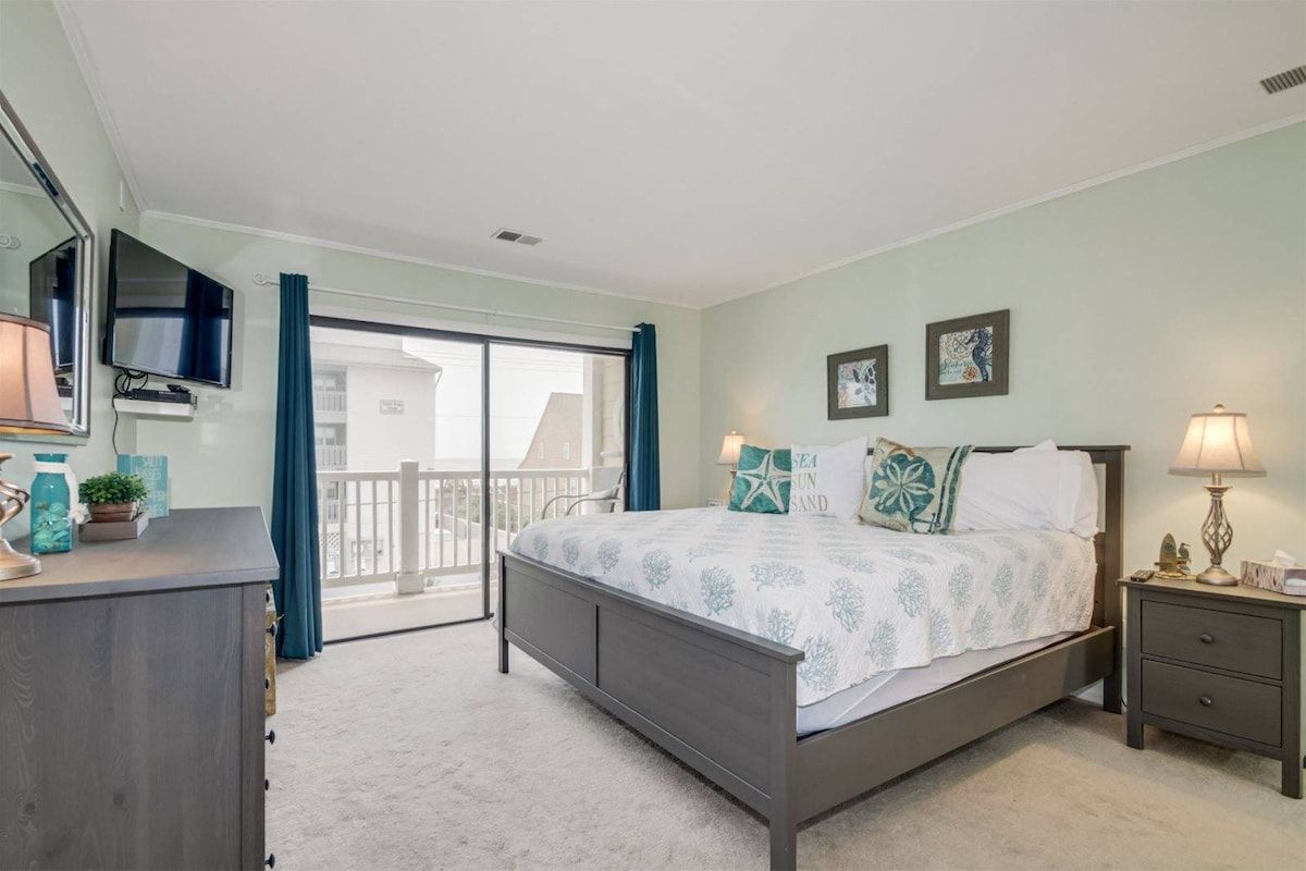 A bedroom with a bed, a dresser, a television, and a balcony.