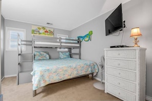 Une chambre d’enfant avec un lit superposé, une commode, un téléviseur et un tableau accroché au mur.