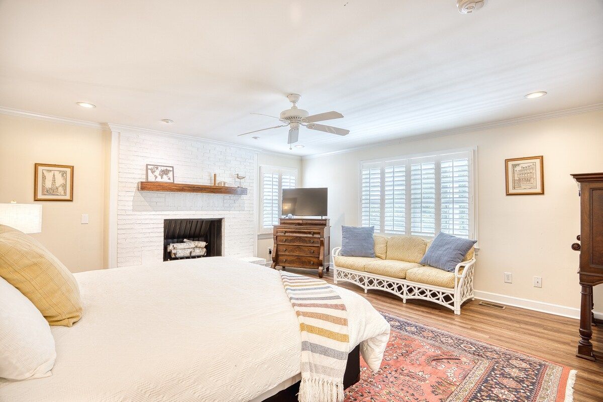 A bedroom with a bed, a fireplace, a television, a sofa, and a ceiling fan.