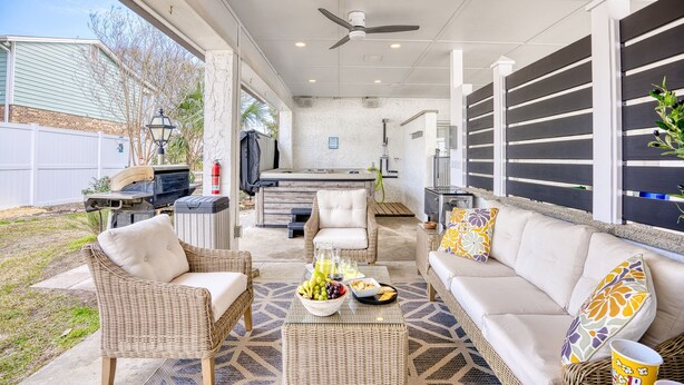 A covered outdoor patio with wicker furniture, a dining table with fruit and snacks, and a barbecue grill. - Seaside Magnolia (North Myrtle Beach)