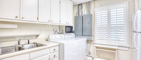 Cocina compacta con armarios blancos, microondas integrado, estufa y refrigerador.
