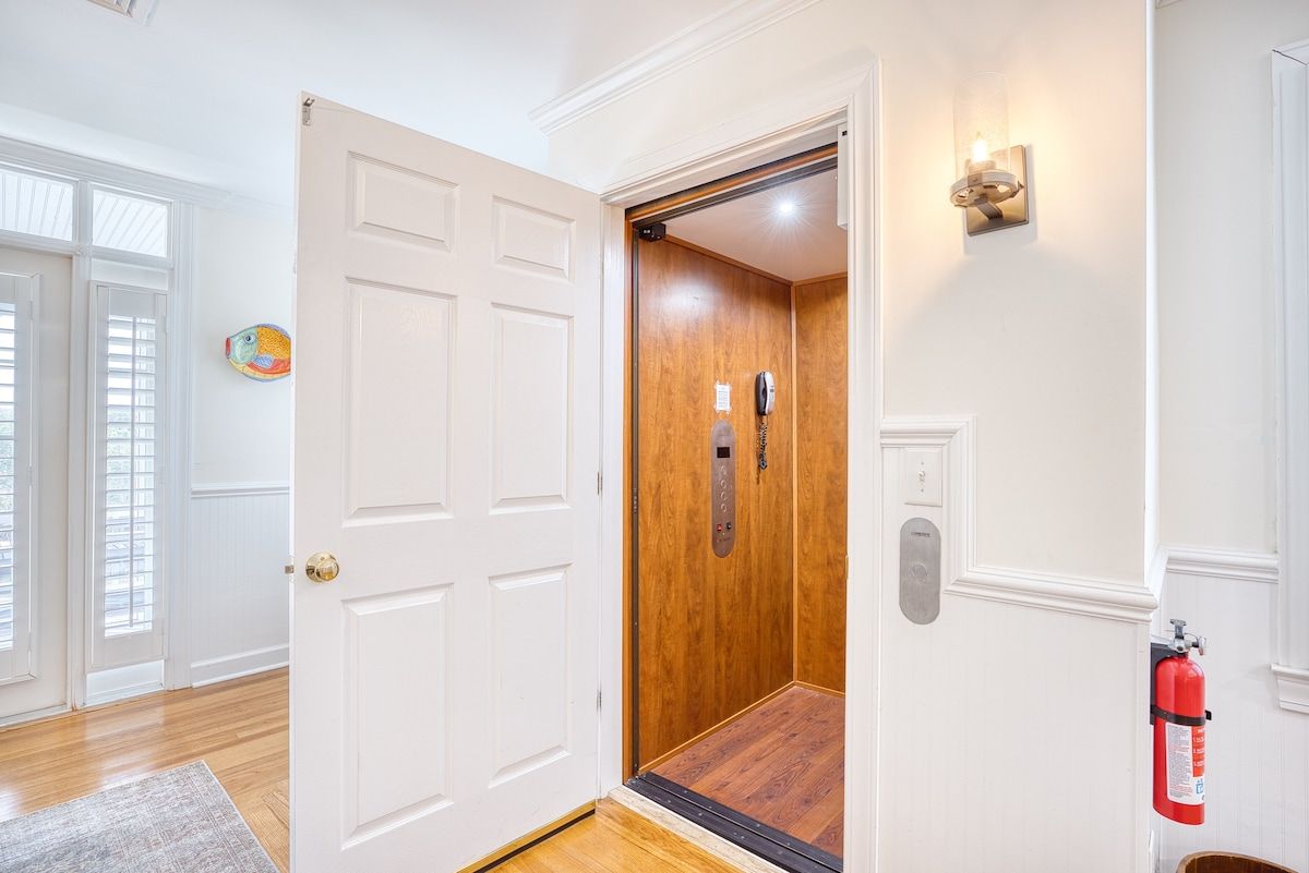 A hallway with a wooden elevator door, a fire extinguisher, and a wall-mounted light fixture.