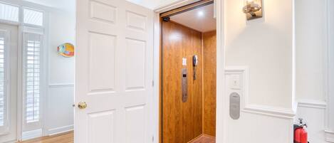 A hallway with a wooden elevator door, a fire extinguisher, and a wall-mounted light fixture.