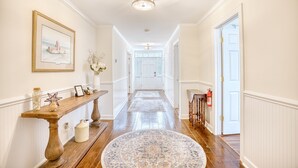 A hallway with a wooden bench, a rug, a framed picture, and a vase with flowers. - Seaside Magnolia (North Myrtle Beach)