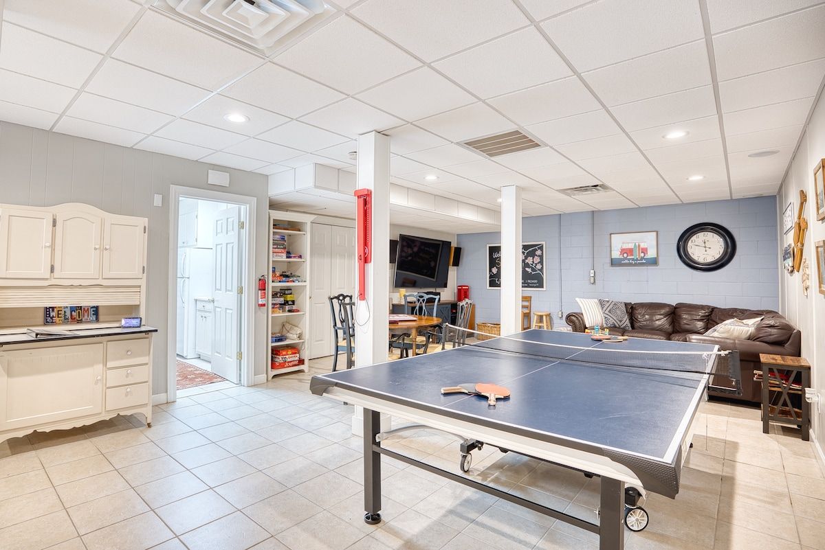 Una habitación con mesa de ping pong, sofá, televisor y un reloj en la pared.