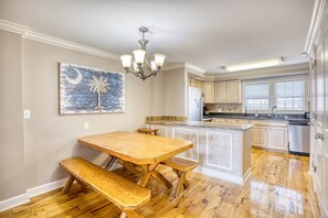 Una cocina con suelo de madera, una mesa de comedor de madera con bancos, una araña y un cuadro en la pared.