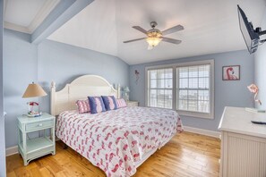 A bedroom with a bed, a ceiling fan, a nightstand, a lamp, a window, and a wall-mounted TV.