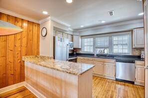 Una cocina con paneles de madera, una isla de encimera de granito y un refrigerador de acero inoxidable.