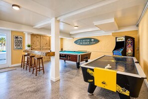 Mesa de bilhar, mesa de futebol de mesa e área de bar com banquetas.