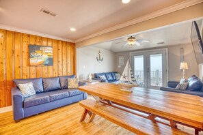 Uma sala de estar com piso de madeira, um sofá azul, uma mesa de jantar de madeira e um ventilador de teto.