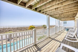 A wooden deck with a pool, white railings, and beach views.