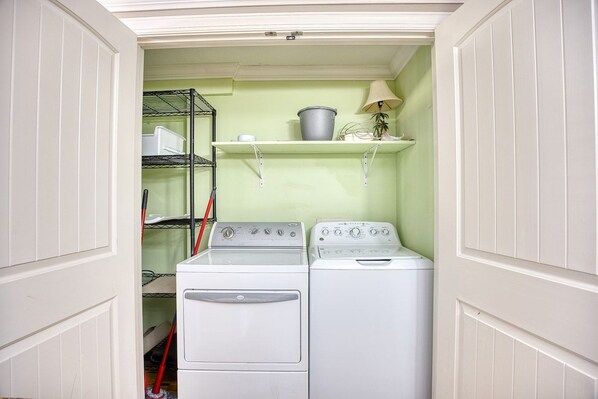 A laundry room with two washing machines, a metal shelf with a bucket, and a mop. - 9BR Oceanfront Home with Pool/Hottub/Gameroom (North Myrtle Beach)