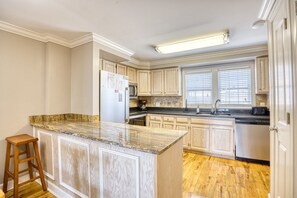 A kitchen with a granite countertop island, wooden cabinets, a stainless steel refrigerator, and a dishwasher.