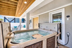 Ein Whirlpool mit Steinfassade, Holzboden und Blick auf einen Garten mit Tisch und Stühlen.