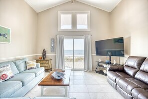 A living room with a sofa, a coffee table, a television, and a view of the beach through a sliding door.