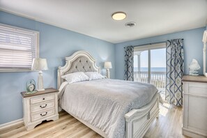 A bedroom with a bed, bedside tables, a window with curtains, and a view of the outdoors.