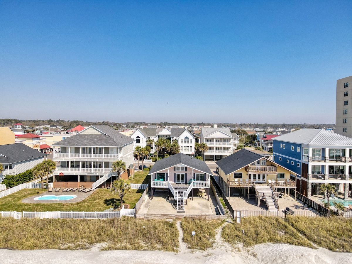 Een woongebied aan de kust met meerdere tweelaags huizen, een zwembad en een strand op de voorgrond.