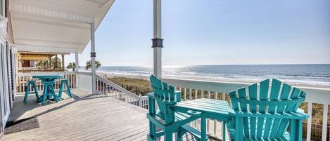 A wooden deck with a table and chairs, overlooking a beach.