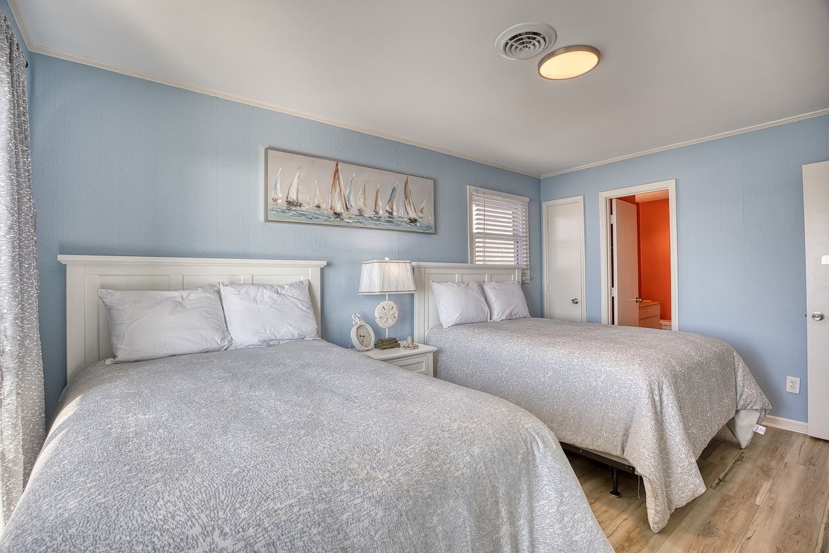 A bedroom with two beds, a painting on the wall, and a door leading to another room.