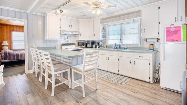 A modern kitchen with white cabinetry, a central island with bar stools, a ceiling fan, and a refrigerator.