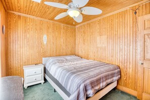 A bedroom with a single bed, a nightstand, a ceiling fan, and wooden walls.