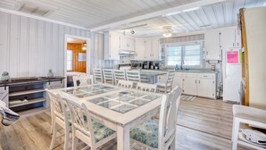 A spacious kitchen with white cabinets, a dining area with a glass-top table, and a wooden floor.