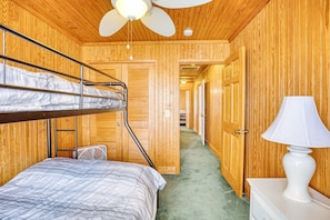 A bunk bed room with a ceiling fan, wooden walls, a bedside lamp, and a carpeted floor. - 4 BR House in Cherry Grove, 1 Block from beach (North Myrtle Beach)