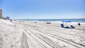 A beach with a clear sky, sandy shore, and a few umbrellas and chairs.