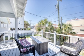 A covered outdoor deck with wicker furniture and a table, surrounded by a white railing and palm trees. - 4 BR House in Cherry Grove, 1 Block from beach (North Myrtle Beach)