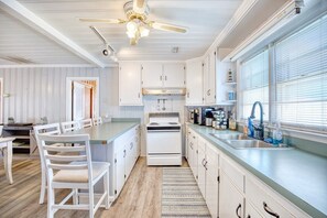 A kitchen with white cabinets, a stove, and a window with blinds.
