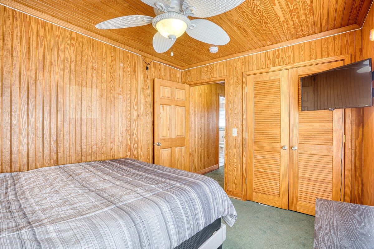 A bedroom with a bed, wooden walls, a ceiling fan, and a TV mounted on the wall.
