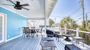 A covered outdoor deck with a ceiling fan, seating area with tables and chairs, and a view of the surrounding area.