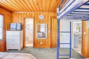 A room with wooden walls, a bed, a dresser, a television, and a door leading to another room. - 4 BR House in Cherry Grove, 1 Block from beach (North Myrtle Beach)
