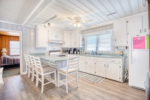 A kitchen with white cabinetry, a central island with seating, a ceiling fan, and a refrigerator. - 4 BR House in Cherry Grove, 1 Block from beach (North Myrtle Beach)